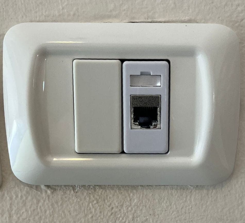 שקע רשת RJ45 לבן מותקן בקיר לצד מפסק תאורה, בתוך מסגרת אחת